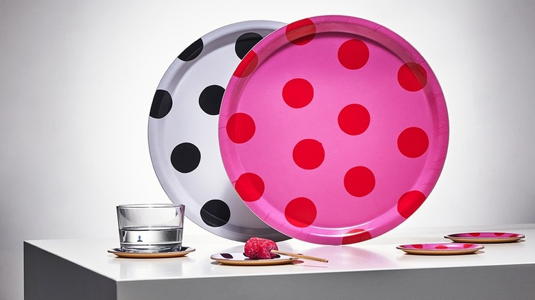 Two large colorful polka dot trays sold at the IKEA Museum sit upright on a neutral table near a glass of water