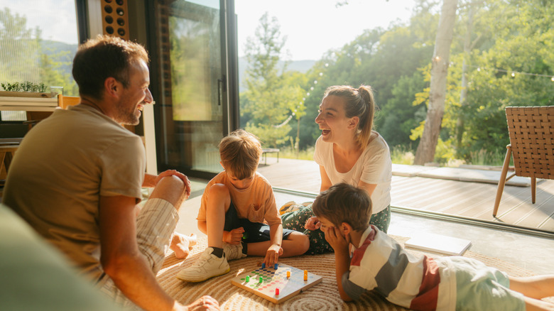 Family of four playing board games on the floor of a modern living room