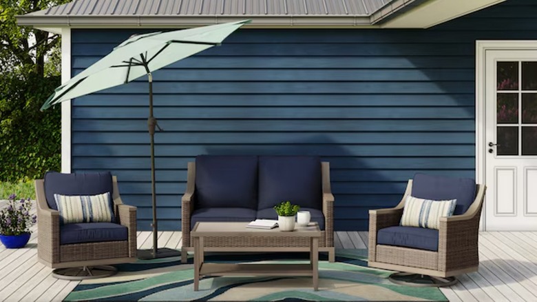 A set of wicker furniture with navy cushions is arranged on a patio in front of a blue house