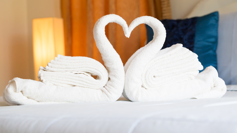 Two bath towel swans facing each other on a bed to form a heart