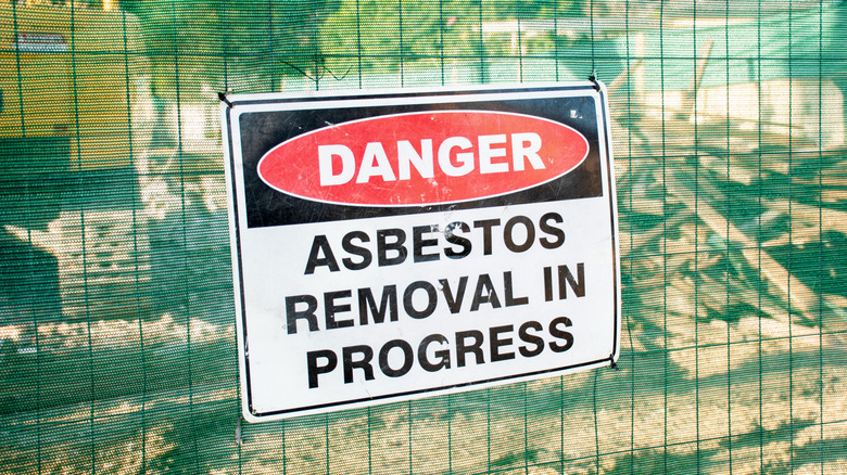 A warning sign about asbestos removal on a sign posted to a fence
