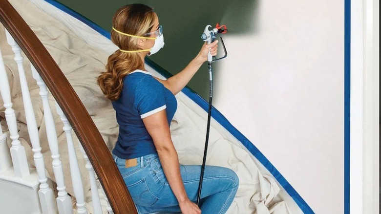 Woman painting wall on stairwell with airless sprayer