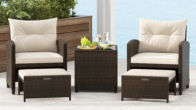 Two wicker chairs with matching ottomans flank a side table laid with snacks