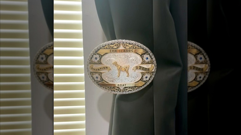 A large vintage belt buckle is used to hold back a black curtain