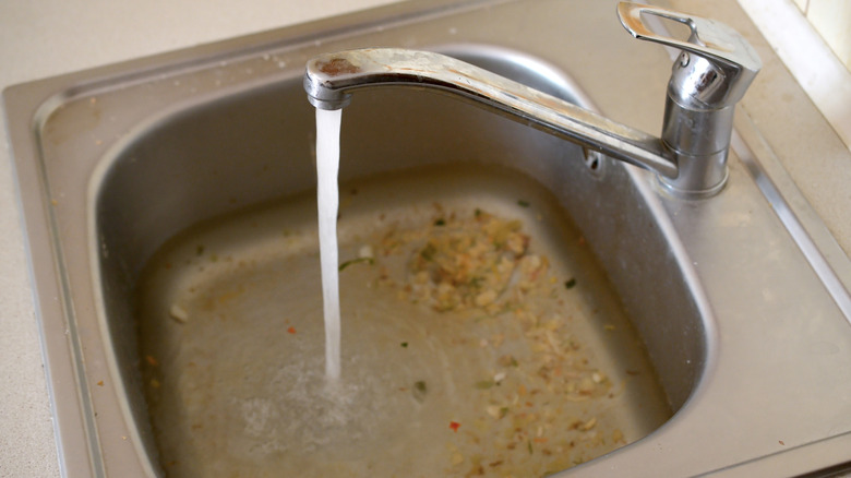 A stainless steel kitchen sink filled with dirty water due to being clogged