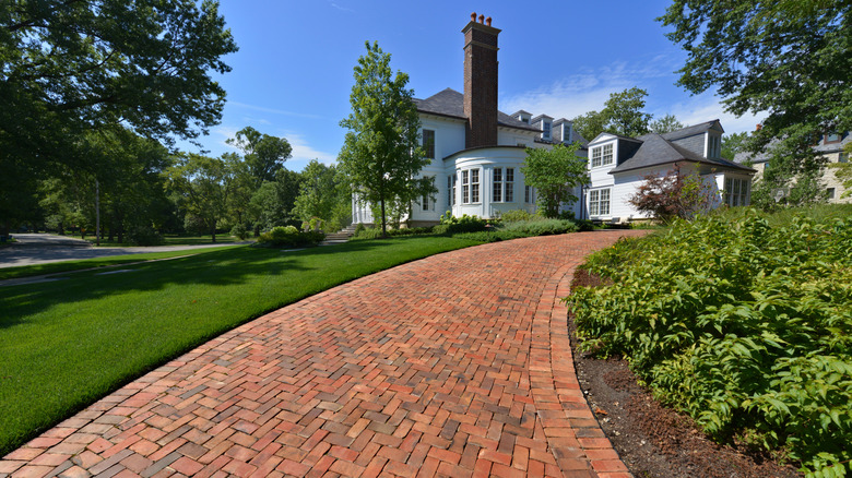 A white stately home with a herringbone brick driveway and manicured landscape