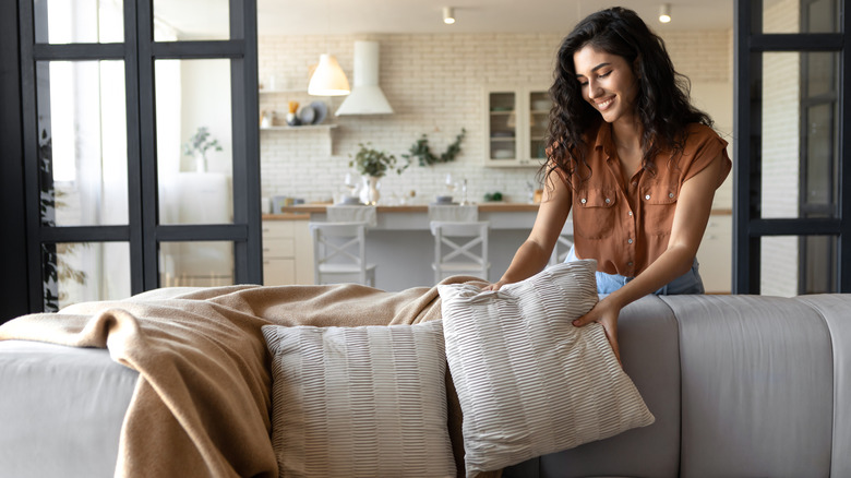 A person placing cream-colored decorative throw pillows on sofa