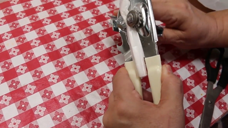 Hands cleaning a can opener with wax paper