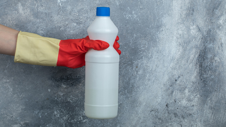 Gloved hand holding a container of bleach
