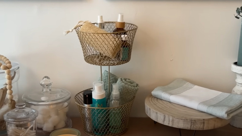 A tiered organization stand sitting on a bathroom shelf.