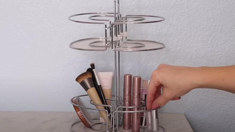 A hand placing make up and brushes into a metal make up stand.