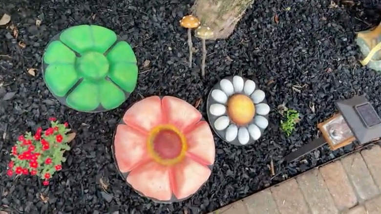 Three colorful flower-shaped stepping stones are arranged in a mulch bed