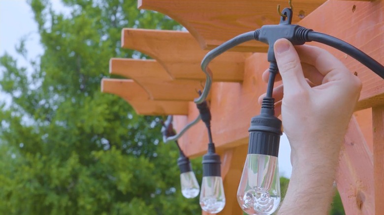 A person installing Enbrighten string lights on a wood pergola