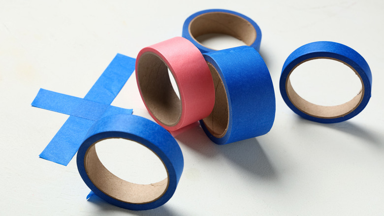 Red masking tape and blue painters tape next to torn tape on ground in X shape