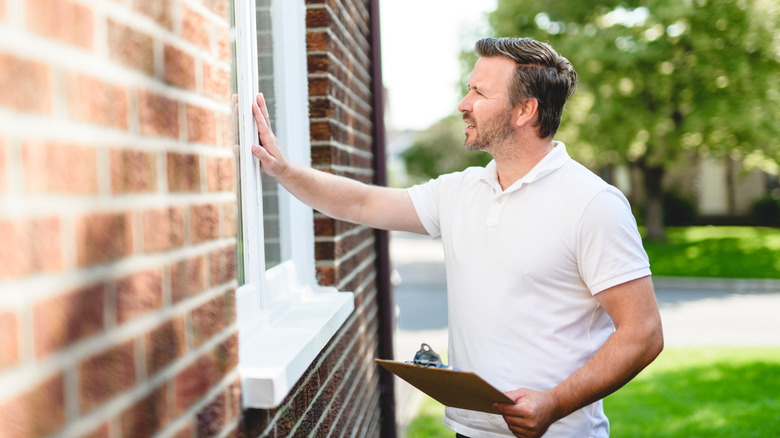 Man inspecting the outside of a house window while holding a clipboard