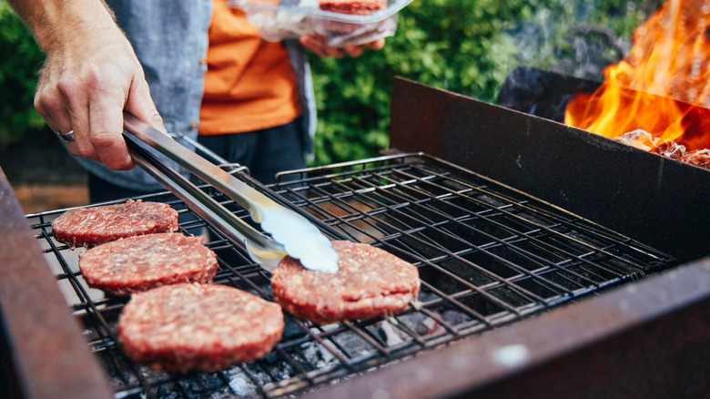 a man uses tongs while grilling patties on a grill