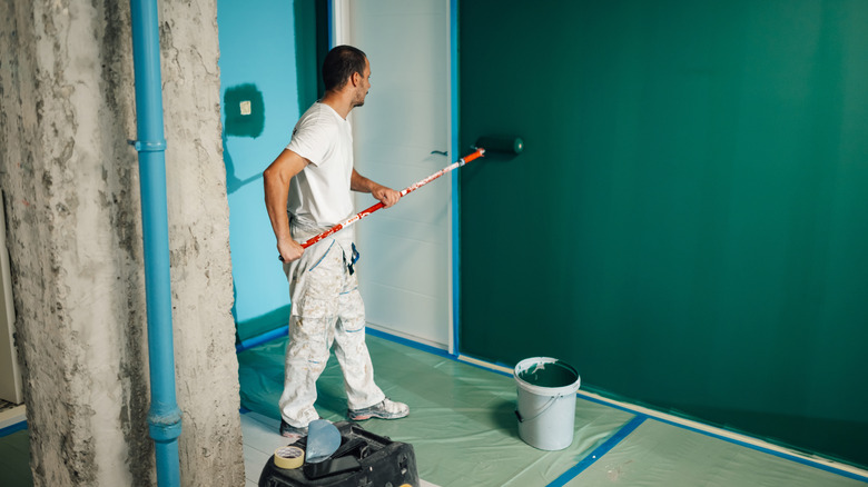 person painting wall a shade of green with extended roller