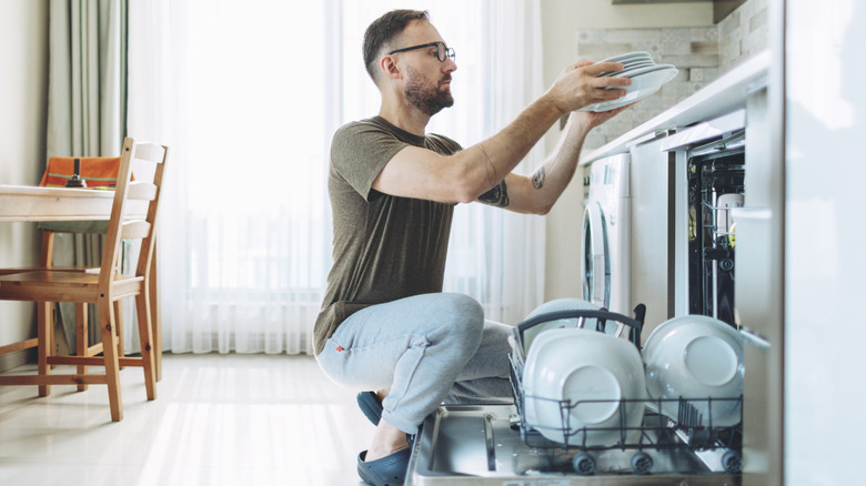 A man unloading clean plates from a dishwasher