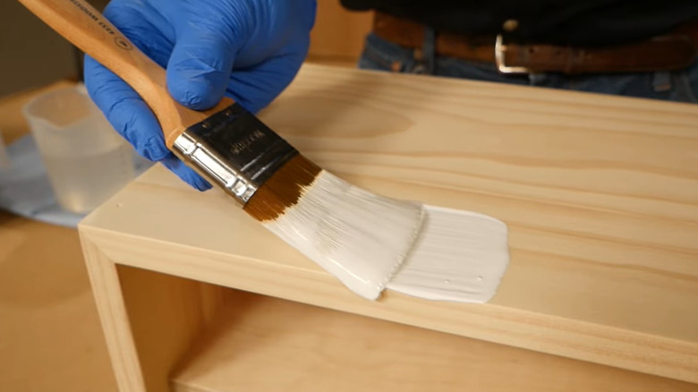 A person in blue globes properly applying paint with a paintbrush