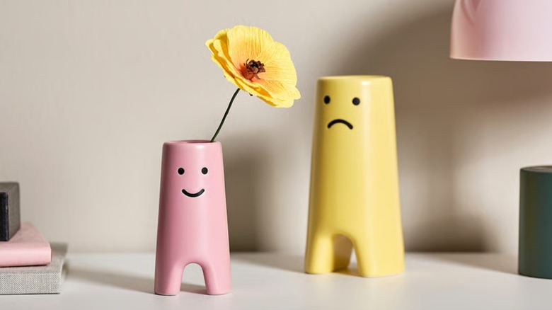 A pink and yellow vase with smiley and sad faces drawn on them
