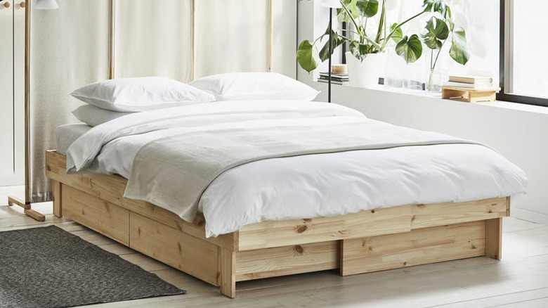 A large wood GLAMBERGET bed frame laden with a mattress, comforter, runner, and pillows