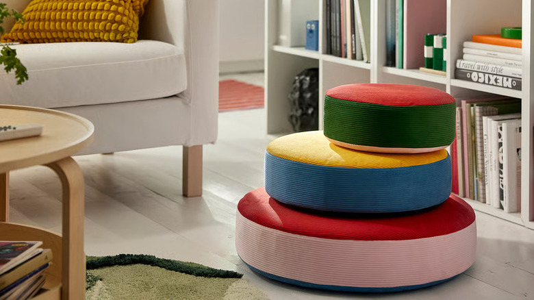 Three brightly-colored GREJSIMOJS Floor cushions sit in a pile on the floor next to a bookshelf