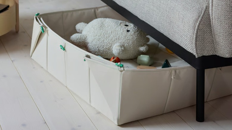 A beige GREJSIMOJS organizer filled with toys under a sofa
