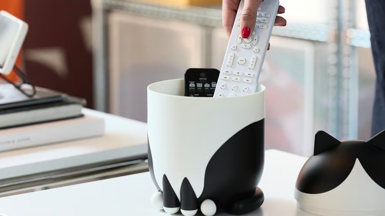 A female hand is pulling a white remote out of a GREJSIMOJS cat-style storage solution