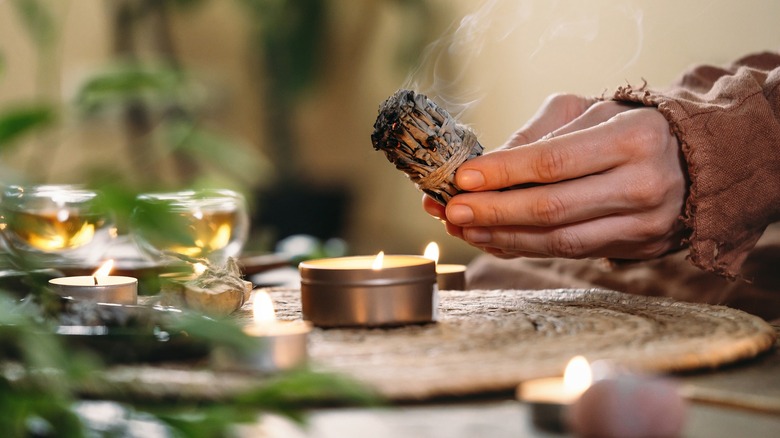 Person burning sage surrounded by candles and tea lights