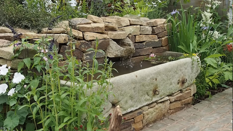A vintage concrete horse trough is used as the basin for a container pond surrounded by plants