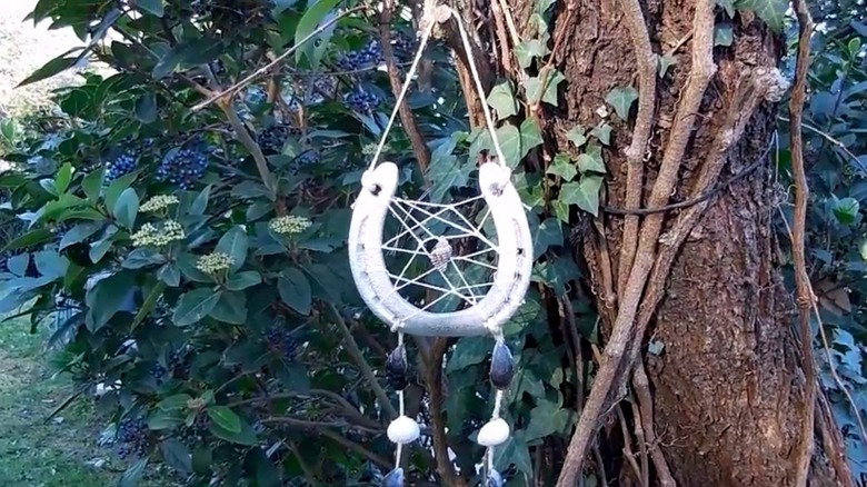 A silver horseshoe transformed into a dreamcatcher hangs from a tree