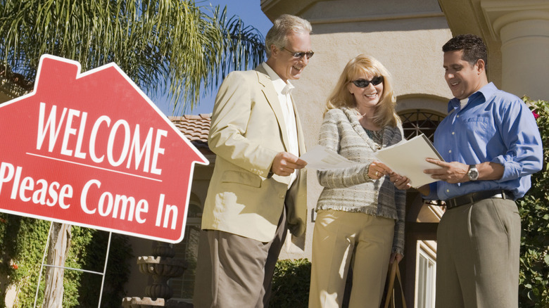a realtor showing an older couple realty papers in front of a california home for sale