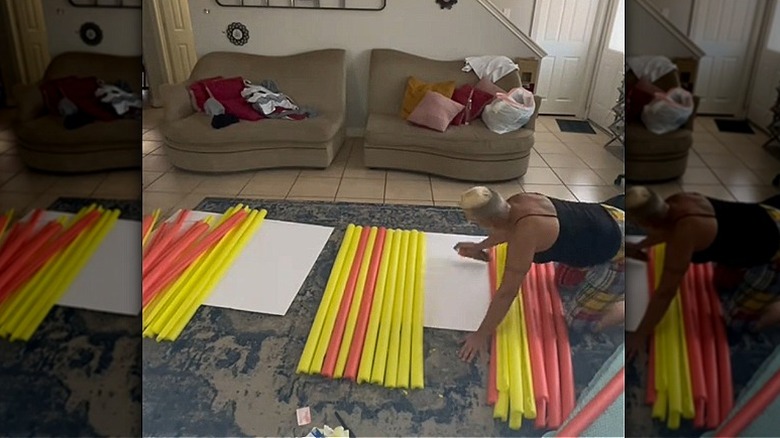 A person sprays glue to posterboard to affix pool noodles.