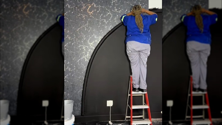 Woman building black marble accent wall with pool noodle, paint, and peel-and-stick on red stepladder