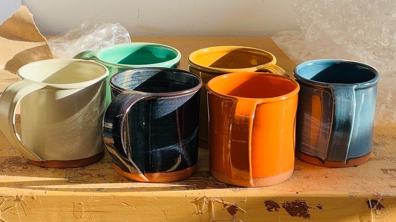 An assortment of colorful New York Stoneware Company mugs sits on a painted table surrounded by bubblewrap
