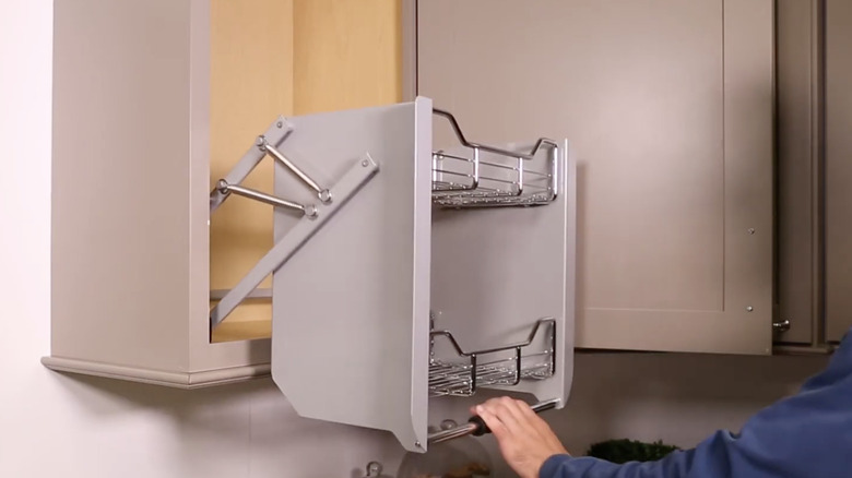 a man's hand reaching for a pull-down cabinet in a kitchen