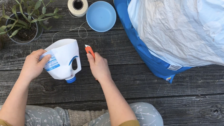Hands holding cut milk jug and box cutter
