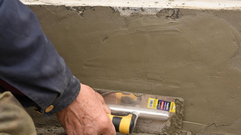 Person filling a gap in a cement wall with plaster