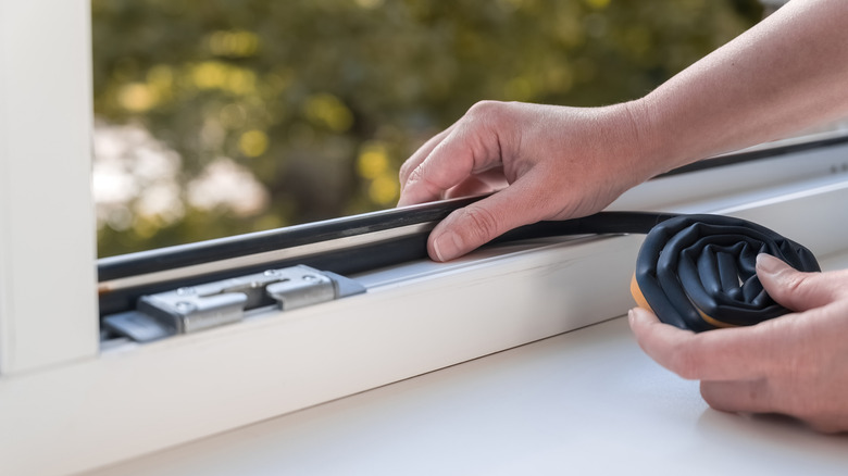 A person installing weatherstripping along the inner edge of a window.