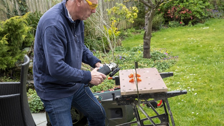 Man sharpening lawn mower blade with an angle grinder