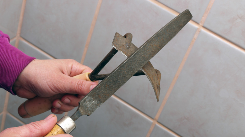 A person preparing to sharpen a small hand hoe with a metal file