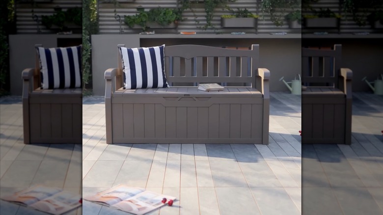 A grey bench box from Devoko on Amazon in grey on an outdoor deck with a blue and white striped pillow