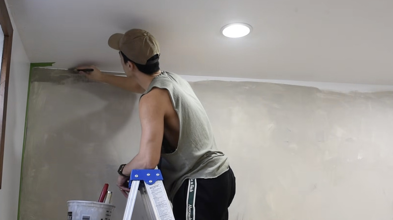 Young man standing on a ladder limewash painting his walls.