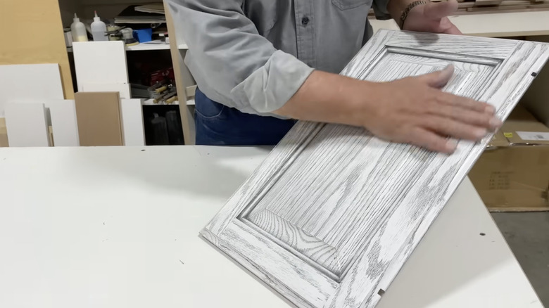 A man putting his hand over a white kitchen cabinet that has just been cerused