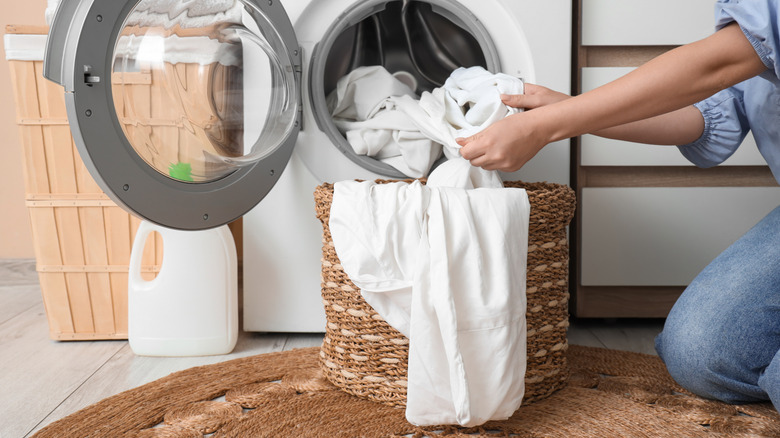 A woman removes white bed sheets from the washing machine.
