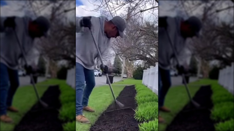A landscaper uses a garden rack to smooth mulch