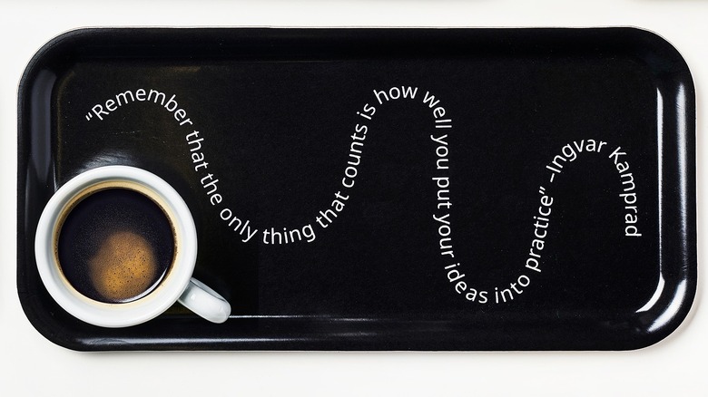 A cup of coffee sits on a black tray with a white Ingvar Kamprad quote that reads "Remember that the only thing that counts is how well you put your ideas into practice."