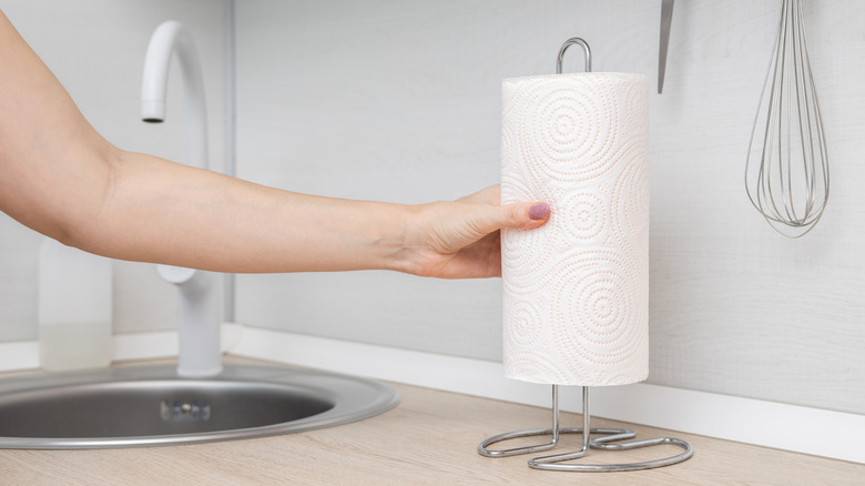 A hand placing a roll of paper towels onto a metal paper towel holding sitting on the counter.