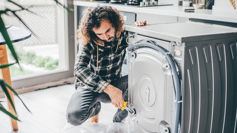 A man repairing a washing machine before installing it.