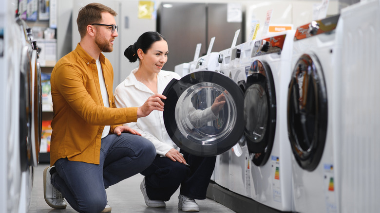 A couple shopping for washing machines at a store.